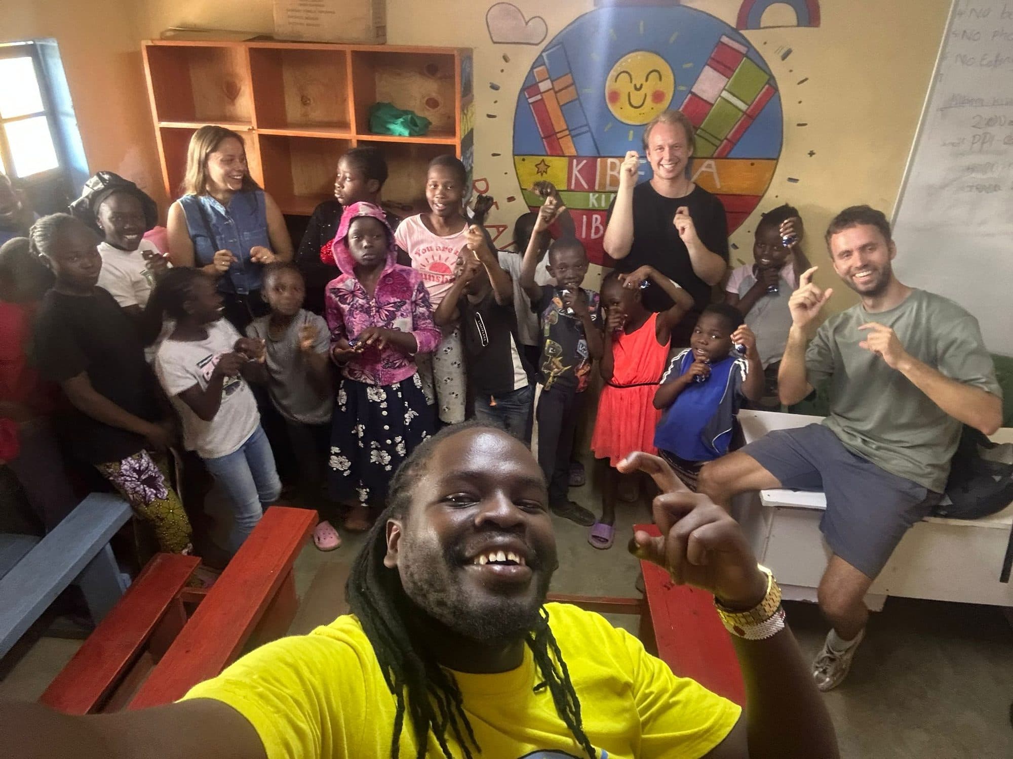Sammy and two guests in the library with a room full of children, the painted logo on the wall behind them